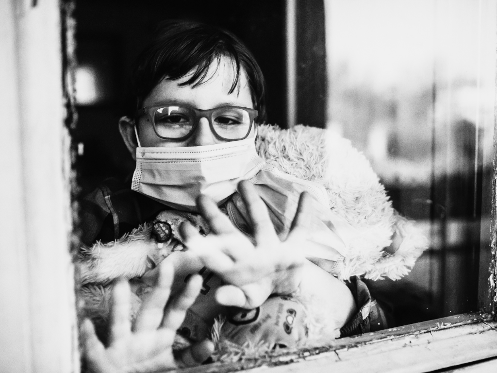 Child with mask through a glass window.