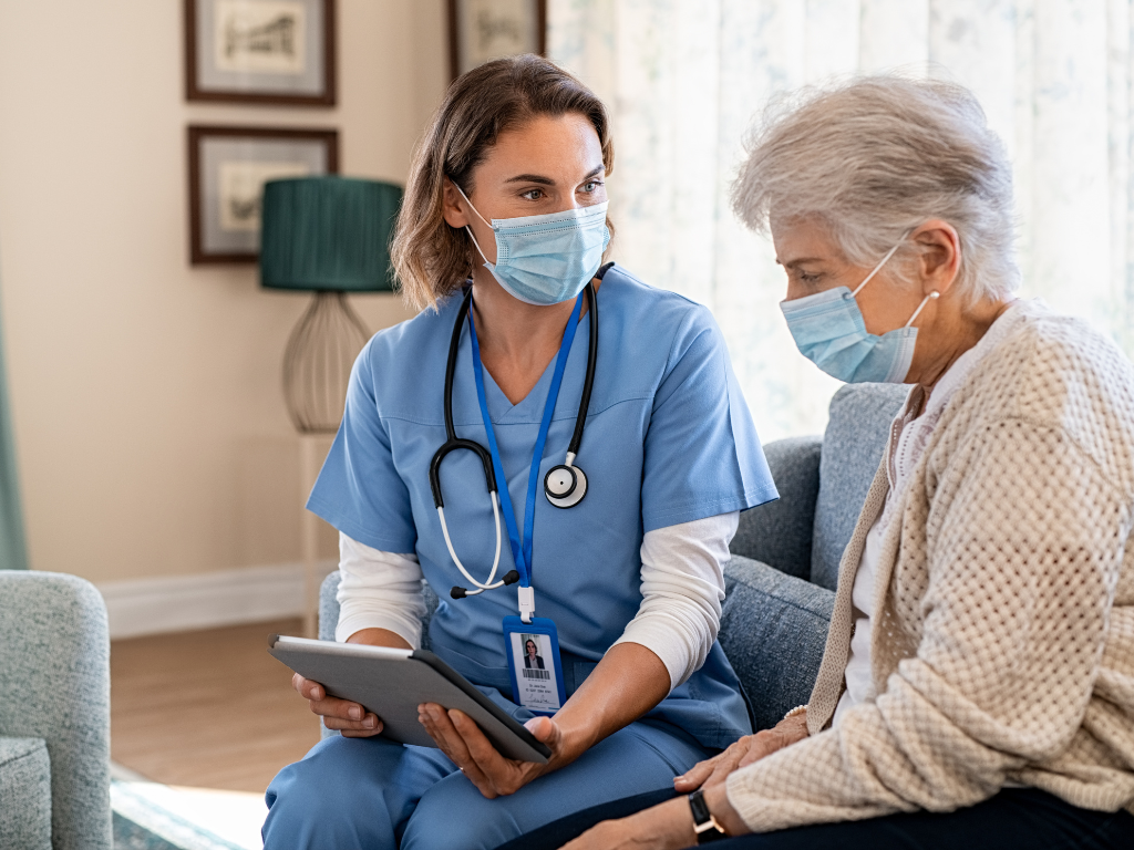 Young female nurse helping an older lady, both are wearing masks.