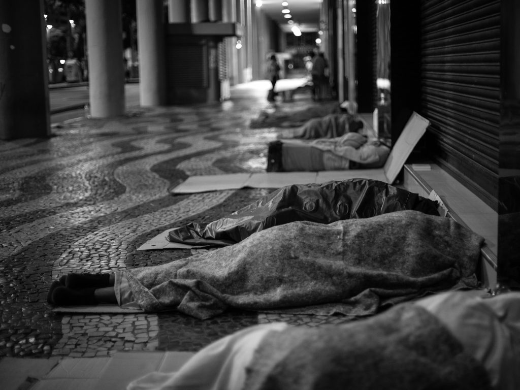 Row of people sleeping beside public building.