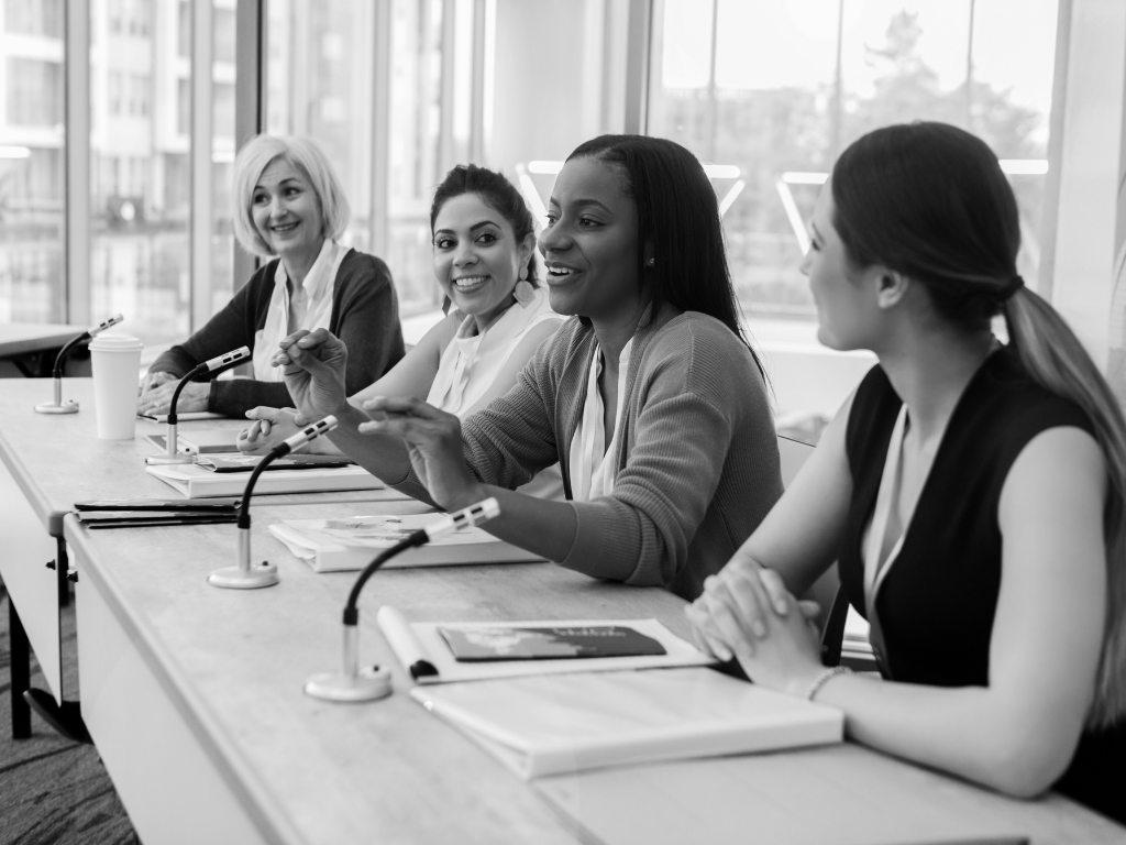 Women in business attire, sitting on a discussion panel.