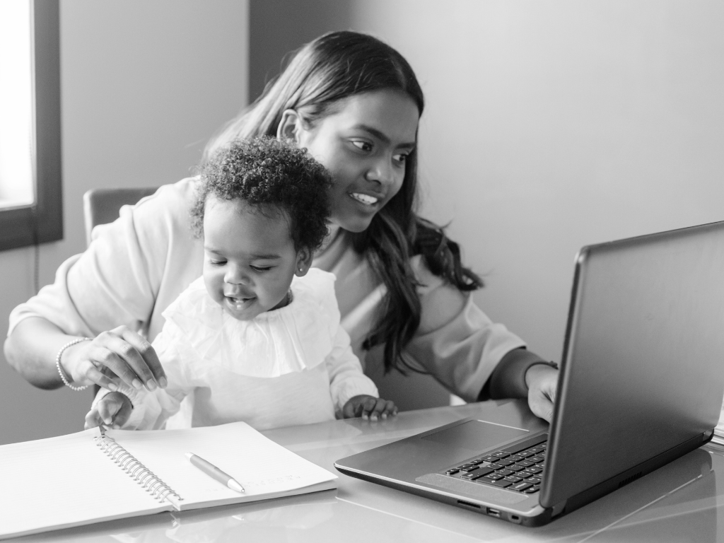 Woman working on a laptop while a toddler sits on her lap.